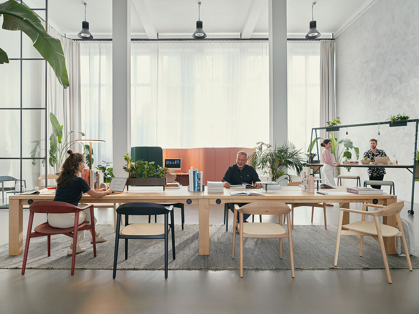 Modern office space with large se:café team table, four people working, and plants on and around the table
