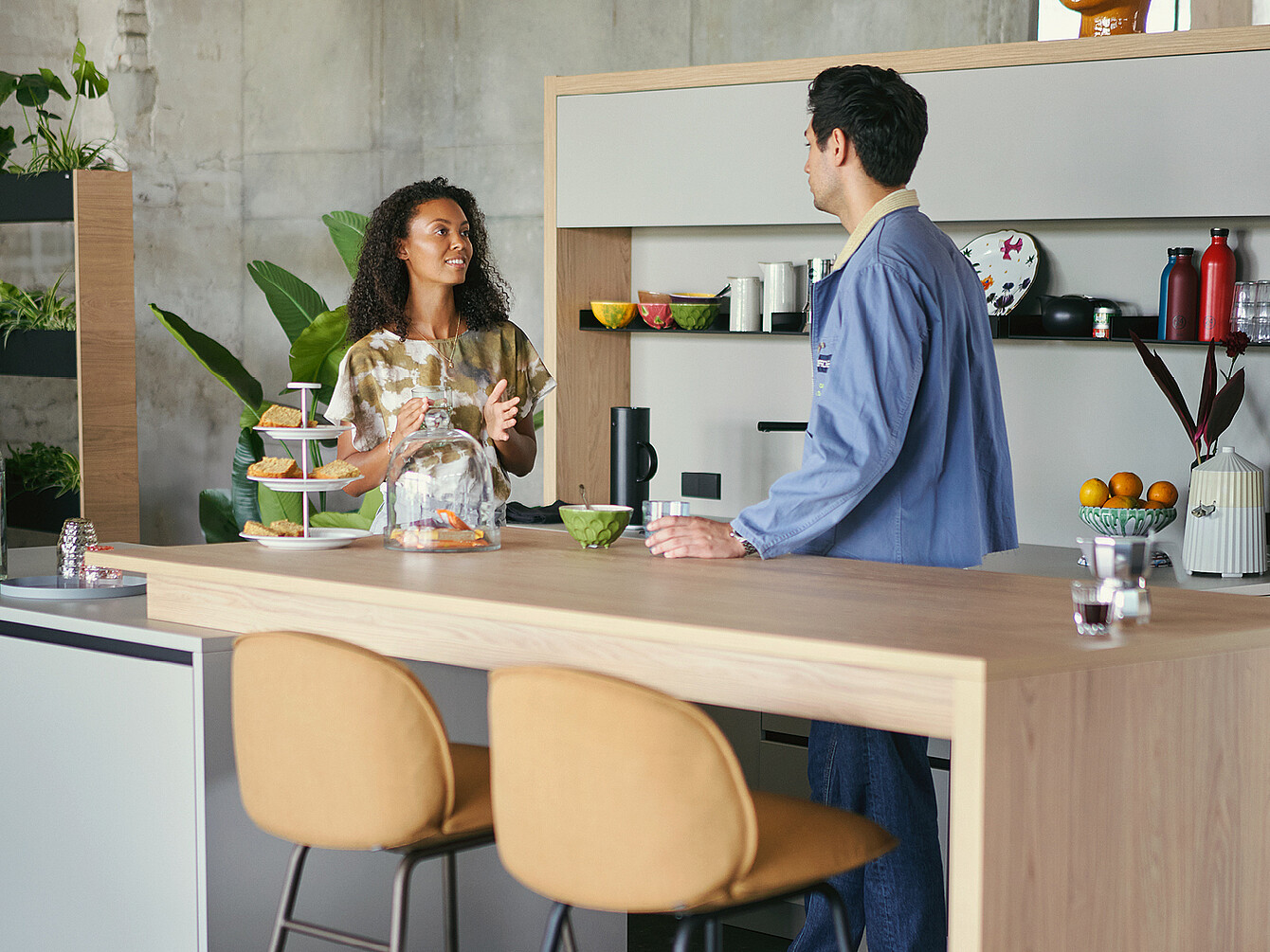 Two employees having a conversation at a modern office kitchen counter with snacks and drinks visible, highlighting intentional in-office interaction.