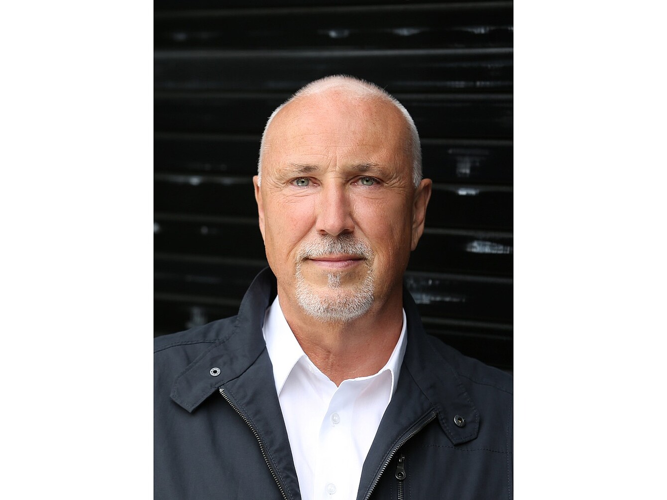 Mann (Jörg Bakschas) mit weißem Hemd und dunkler Jacke vor schwarzem Hintergrund.