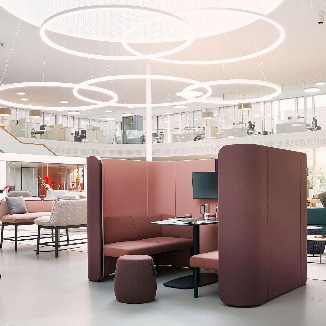 Offener moderner Bürobereich mit flexiblen se:hive Raumlösungen von Sedus, bestehend aus gepolsterten, halbhohen Trennwänden, Sitznischen, Hockern und runden Deckenleuchten, die visuelle Strukturierung und akustische Dämpfung bieten