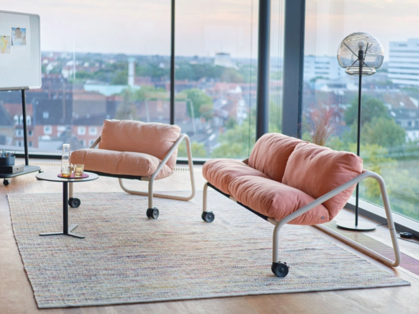 Single-seat and two-seat sofas with metal frames and wheels on a rectangular rug in front of a large window