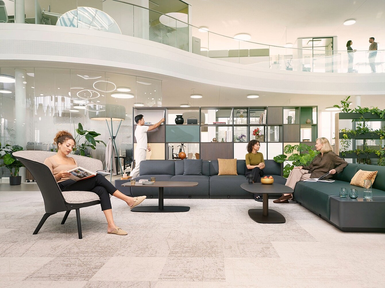 Moderne, offene Bibliothekszone mit Sitzgruppen, Regalen und Personen, die lesen, sich unterhalten und ein Whiteboard nutzen.