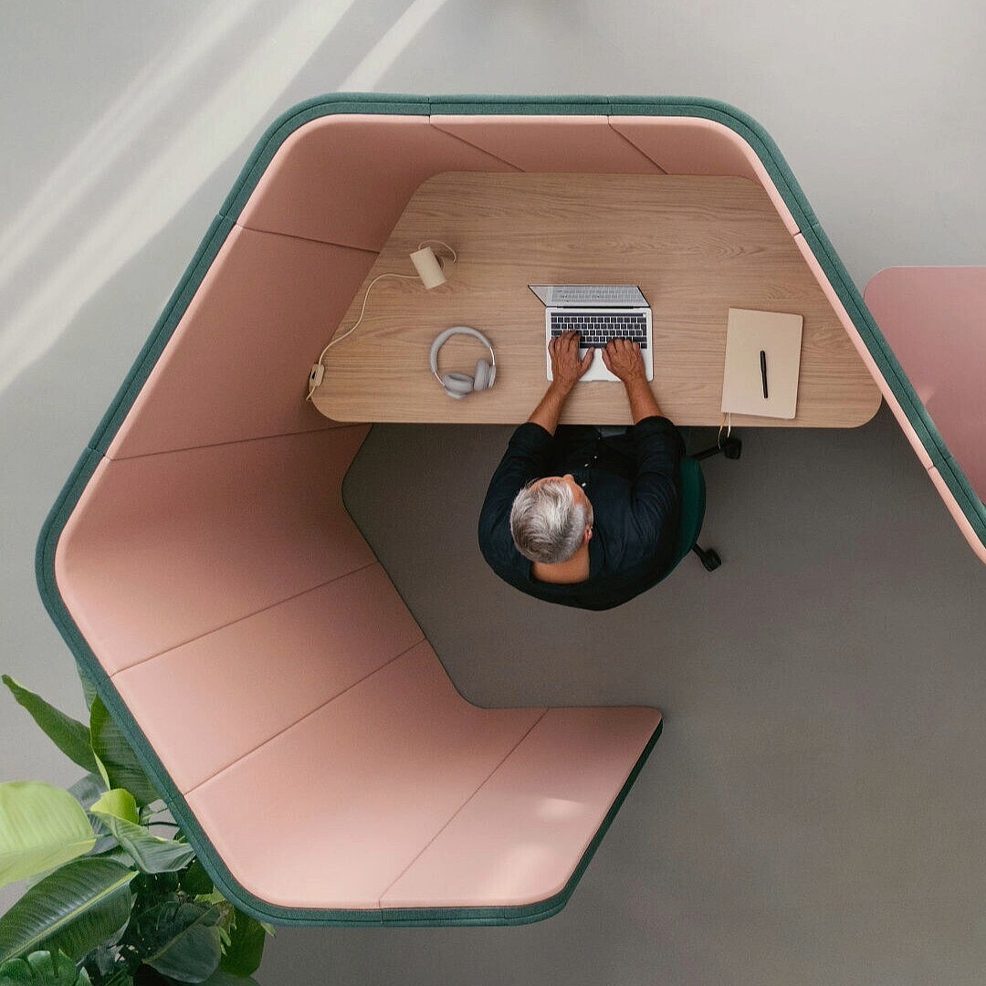 Two people working separately in adjacent hexagonal booth desks with laptops and office supplies