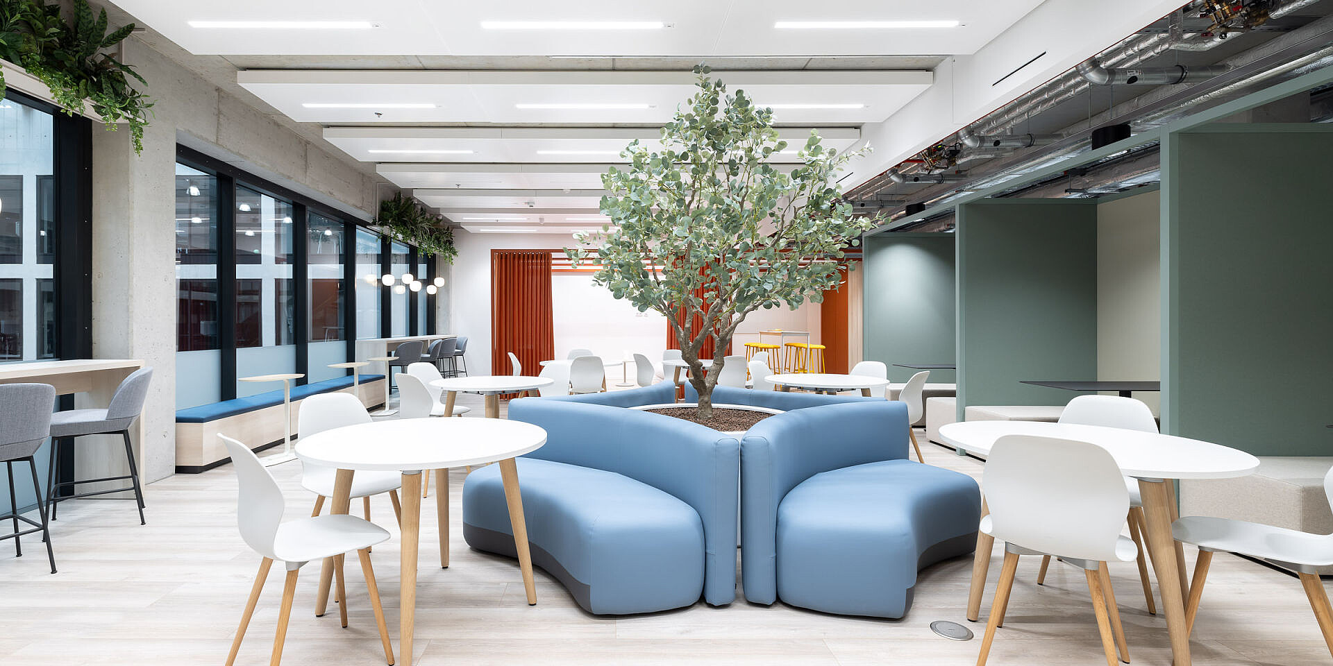 Helle Kantine mit weißen runden Tischen, blauen se:spot Designstühlen und einem zentralen Baum in einem blauen Sitzmöbel, moderne Einrichtung bei Veolia. 