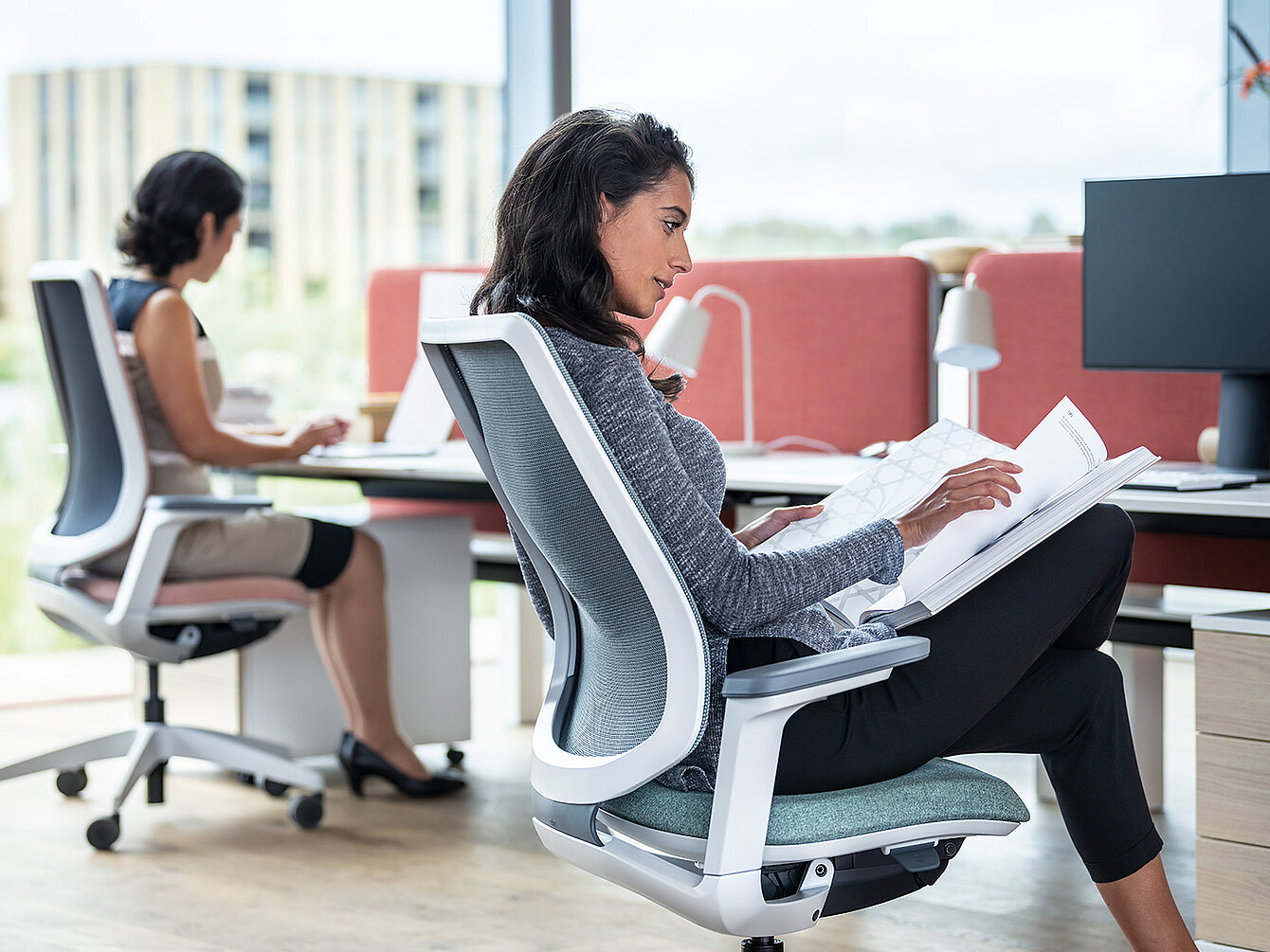 wei Frauen arbeiten in einem modernen Büro, eine liest Dokumente, die andere tippt am Computer