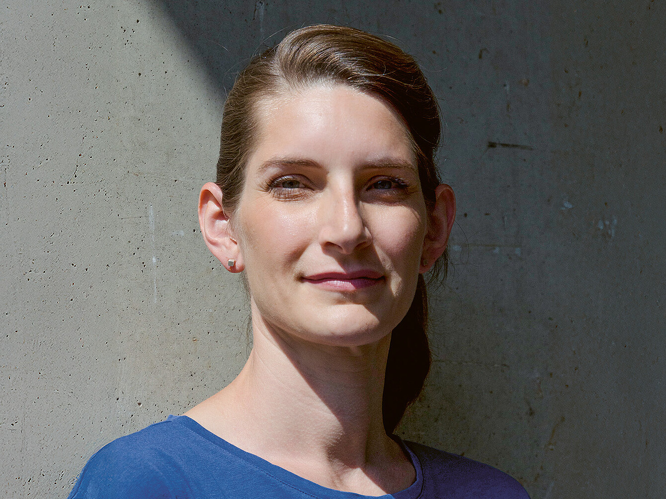 Portrait of industrial designer Judith Daur, smiling confidently against a textured concrete background, wearing a blue top.