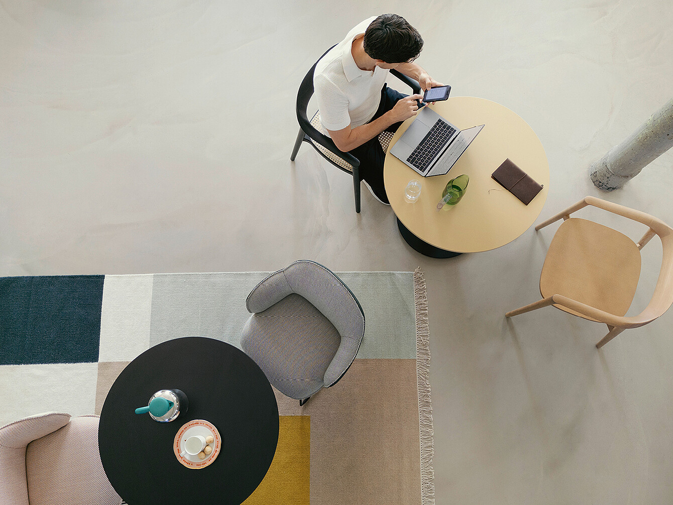 Person sitzt an rundem Tisch mit Laptop und Smartphone in moderner Bürobibliothek, Raum für konzentriertes Arbeiten und Ruhe