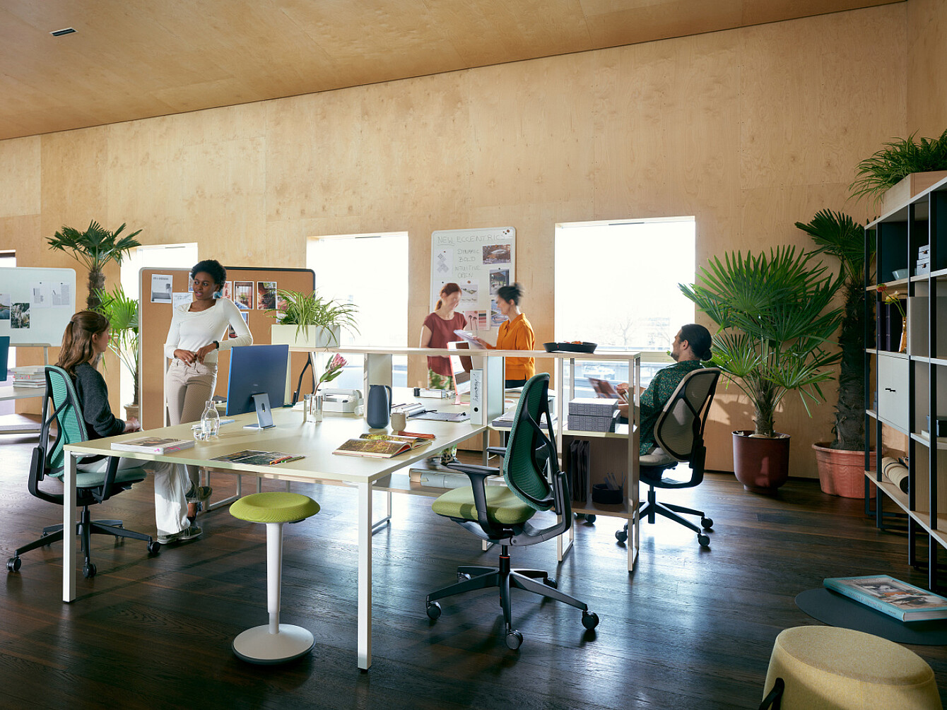 Open office with natural light, plants, ergonomic chairs, and employees collaborating, reflecting a workplace focused on wellbeing and holistic support.