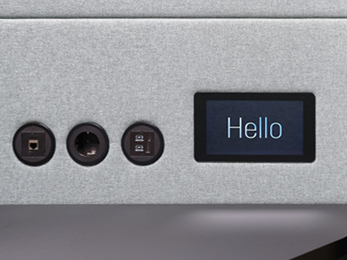 Close-up of a device panel showing three circular ports and a small rectangular touch display with the word 'Hello'.