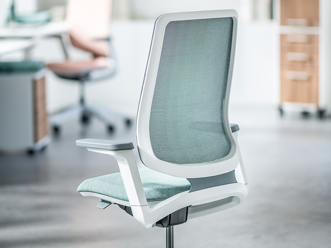 Moderner ergonomischer Bürostuhl mit hellgrauem Netzrücken und verstellbaren Armlehnen in einem Büro