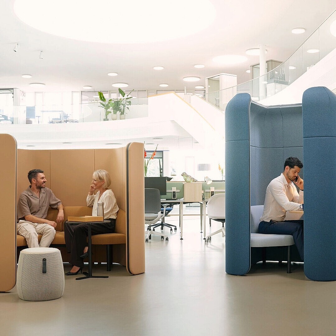 Zwei Personen sitzen jeweils in separaten, modularen Rückzugsorten se:hive in einem offenen, hellen Büro mit Pflanzen und moderner Einrichtung.