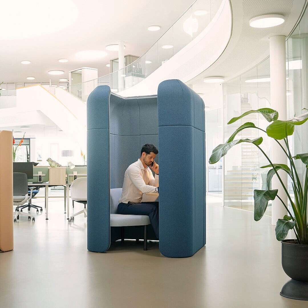 Zwei Personen sitzen jeweils in separaten, modularen Rückzugsorten se:hive in einem offenen, hellen Büro mit Pflanzen und moderner Einrichtung.