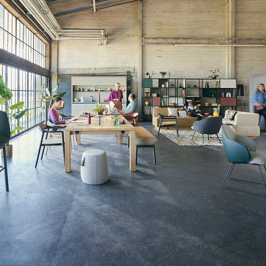 Hub Work Café office space with people working and collaborating at tables and seating areas, featuring large windows and industrial design