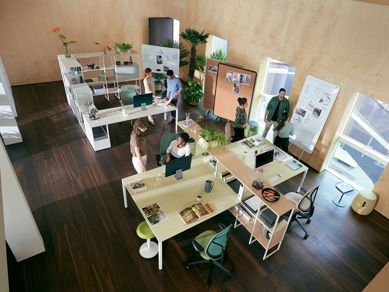 Büro mit modularen, offenen Arbeitsplätzen, mehreren Personen im Gespräch und Pflanzen als Raumteiler