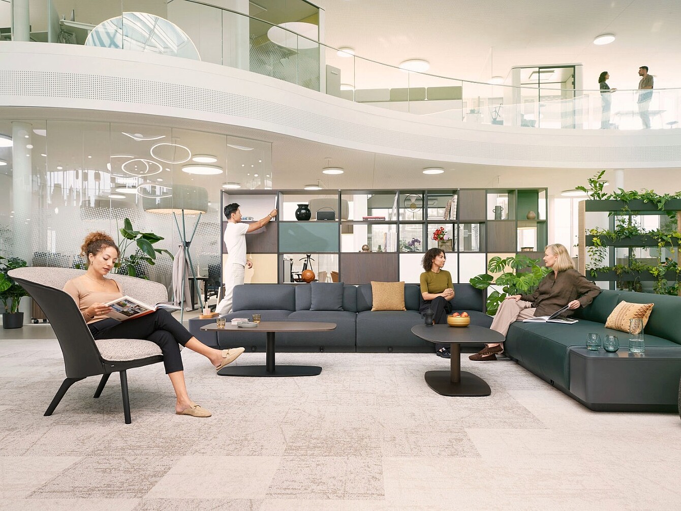 Modern lounge area with modular sofas, armchair, low tables, shelving units, and people engaged in conversation and activity