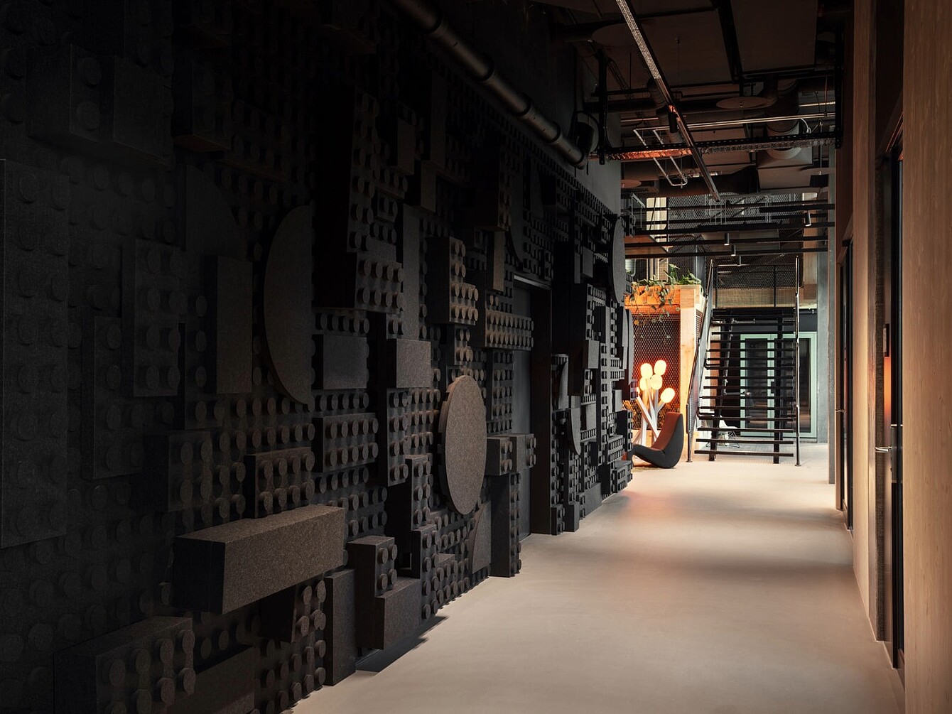 Langer Flur im Novu Campus mit schwarzer, strukturierter Wandgestaltung aus modularen Elementen und moderner Beleuchtung am Ende des Gangs.