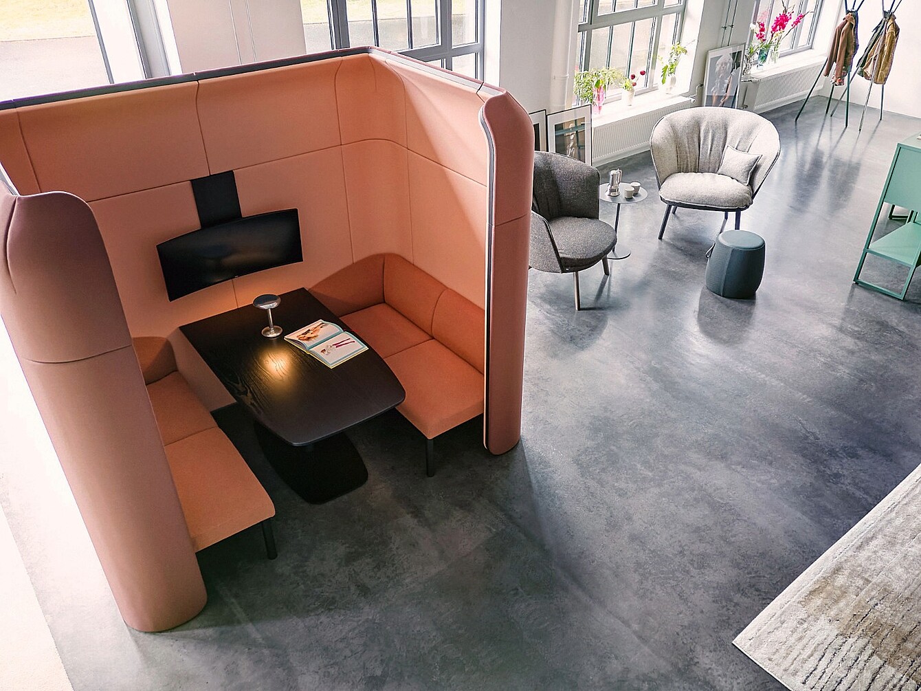 Offener Raum mit flexibler se:hive Sitznische aus gepolsterten Wandelementen und Sitzbänken, daneben zwei gepolsterte Sessel mit kleinem Tisch auf glattem Boden vor großen Fenstern