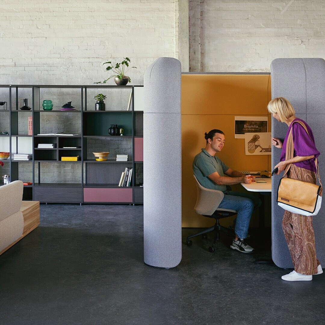 Open office landscape with seating area, room divider and employees in conversation.