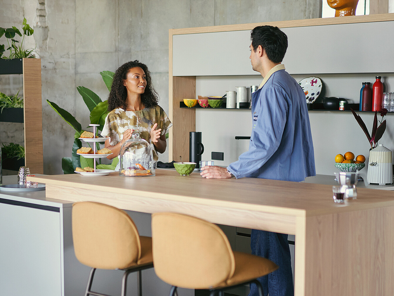 Two employees talking at a wooden counter in a work café with plants and kitchen items around, illustrating a flexible work environment.