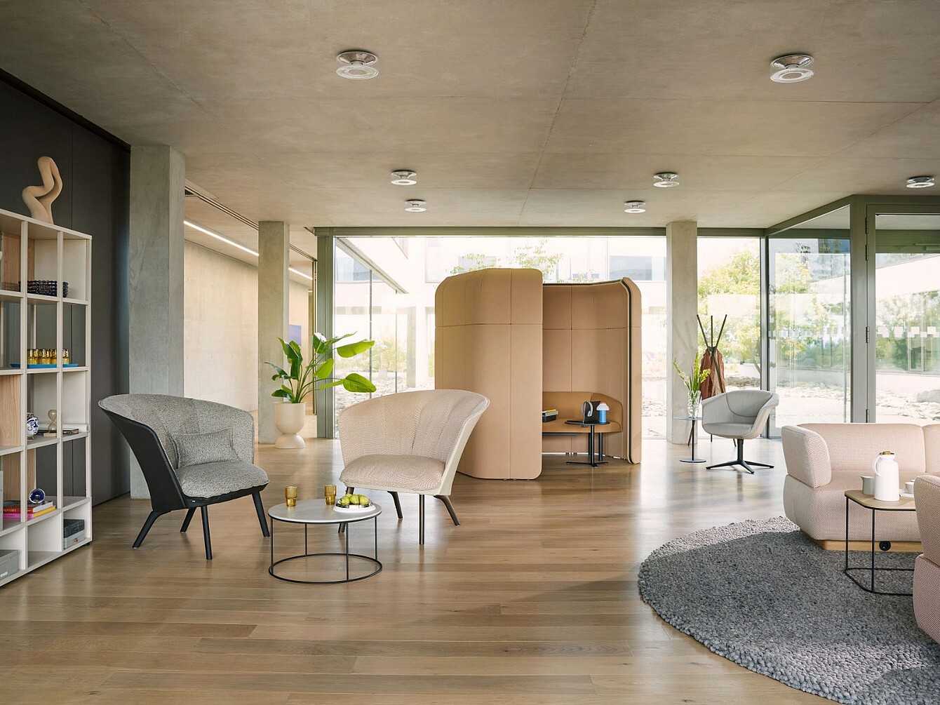 Modern open office space with multiple armchairs around small tables and a curved privacy pod in the background