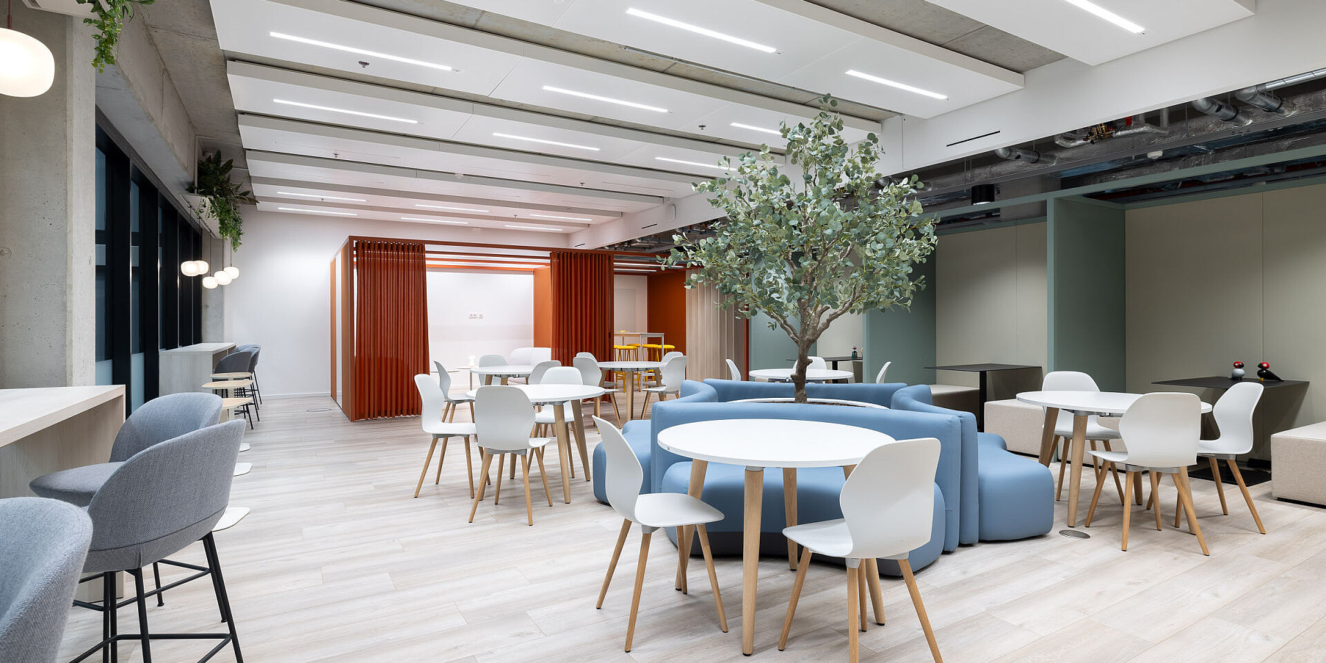 Moderner Bistro-Bereich bei Veolia mit runden se:assist Tischen und ergonomischen se:spot Designstühlen in hellen Farben, umgeben von Sofas und einer großen Pflanze für entspannte Pausen. 