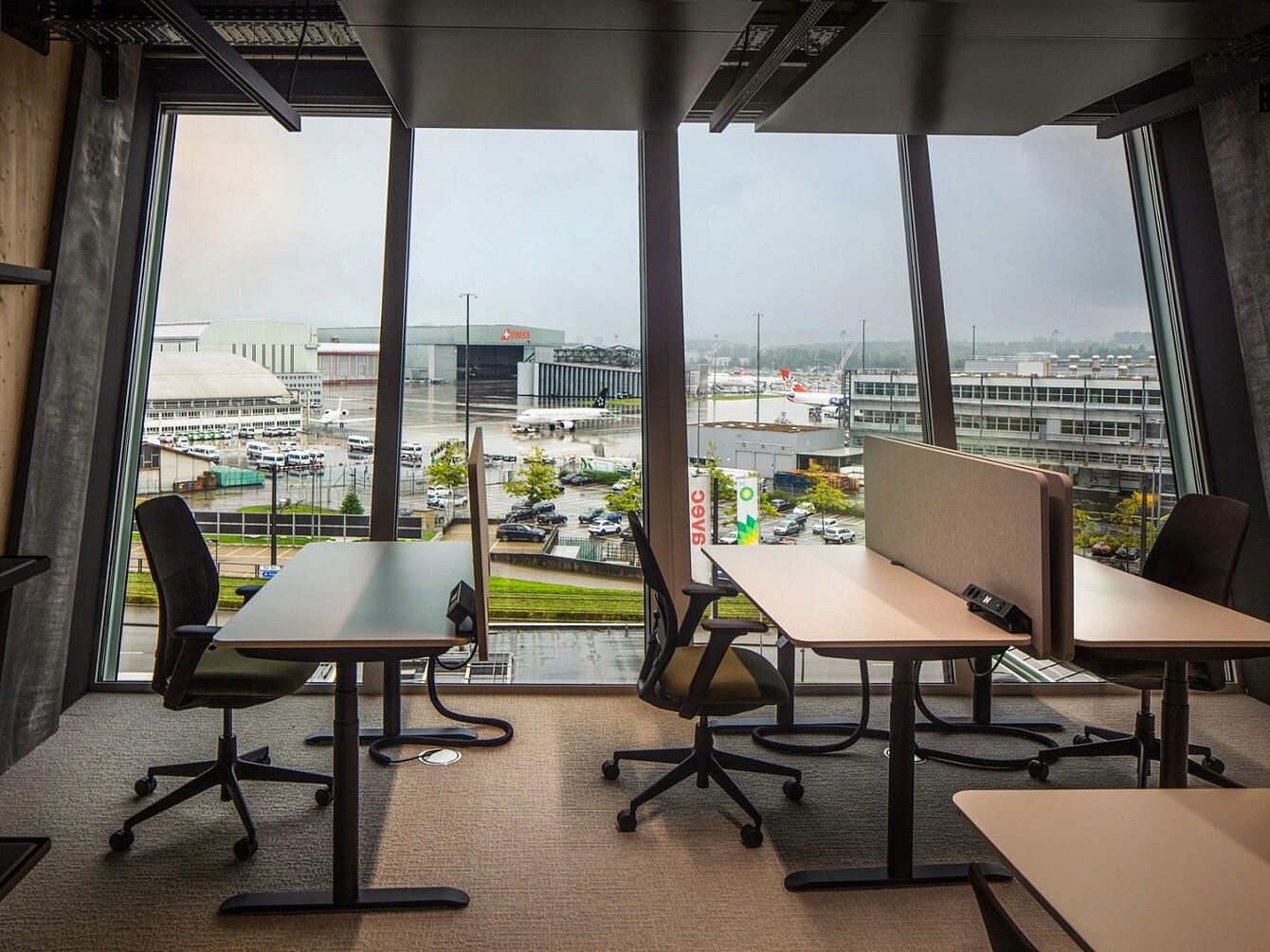 Blick aus einem Büro mit Sedus-Bürostühlen und Tischen auf den Flughafen Zürich mit mehreren Flugzeugen und Gebäuden im Hintergrund.