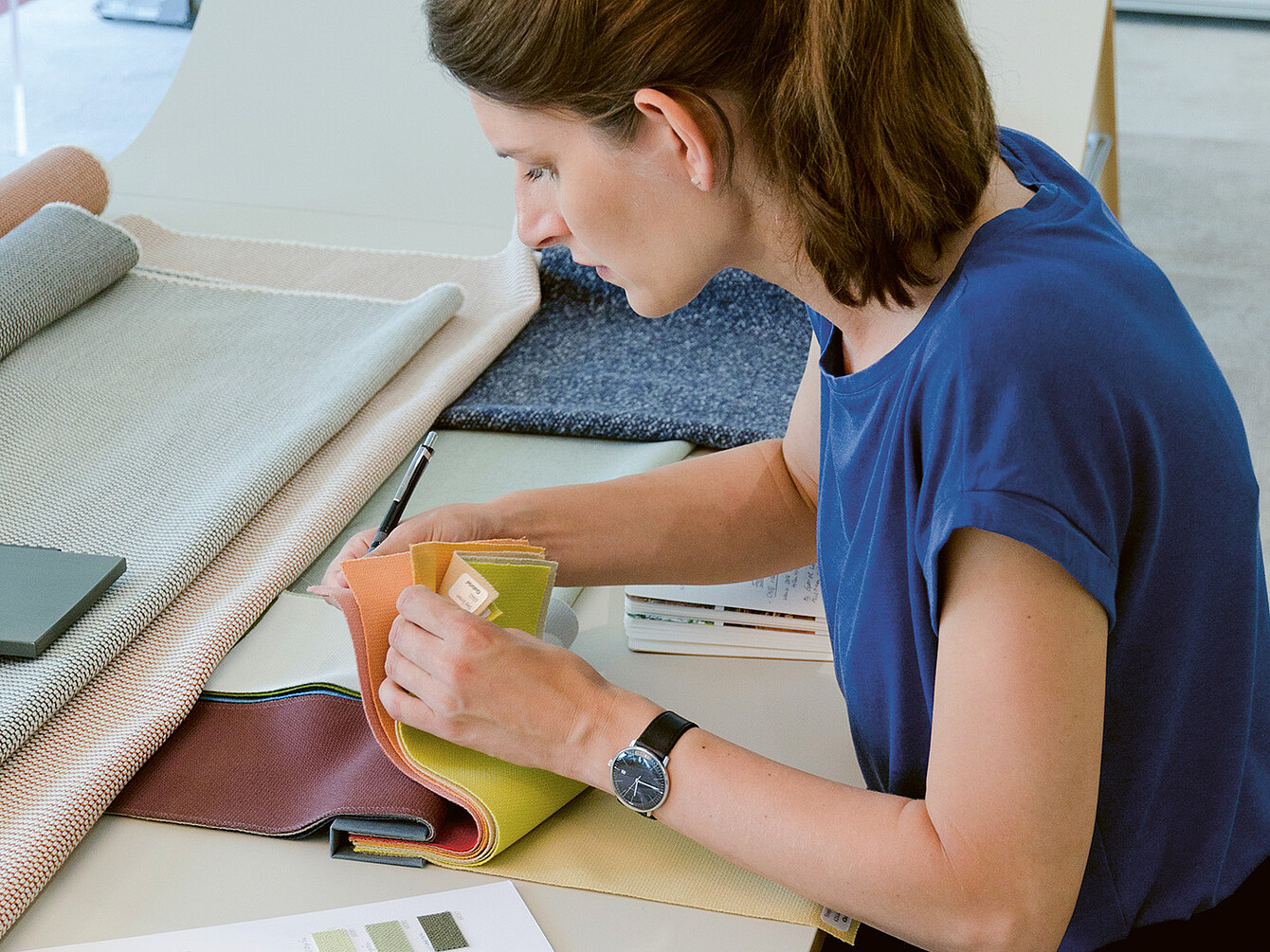 Industrial designer Judith Daur examines fabric swatches, focusing on color and texture, in a workspace filled with various materials.