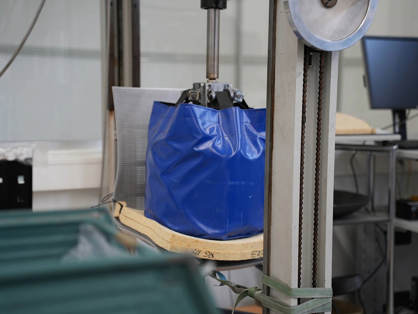 Blue bag suspended in a mechanical testing device with a wooden base and metal frame in a laboratory setting