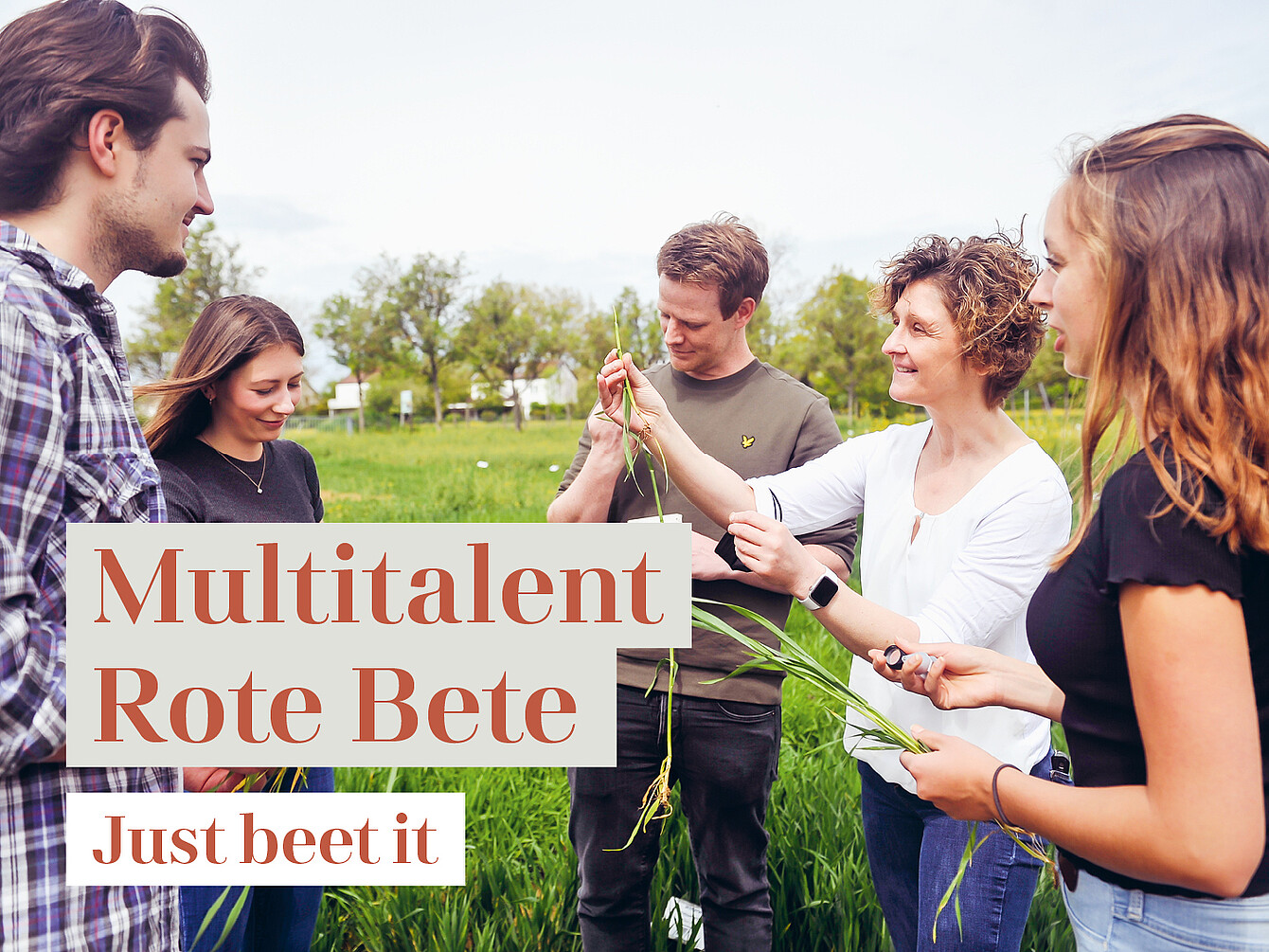 Mehrere Personen stehen im Freien auf einer Wiese und halten frische Rote-Bete-Pflanzen mit Blättern in den Händen.