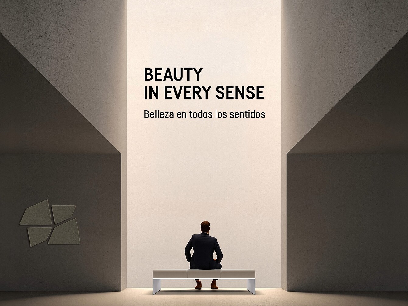 Ein Mann in dunklem Anzug sitzt auf einer weißen Bank vor einer hohen, hell erleuchteten Wand mit dem Text 'BEAUTY IN EVERY SENSE Belleza en todos los sentidos'