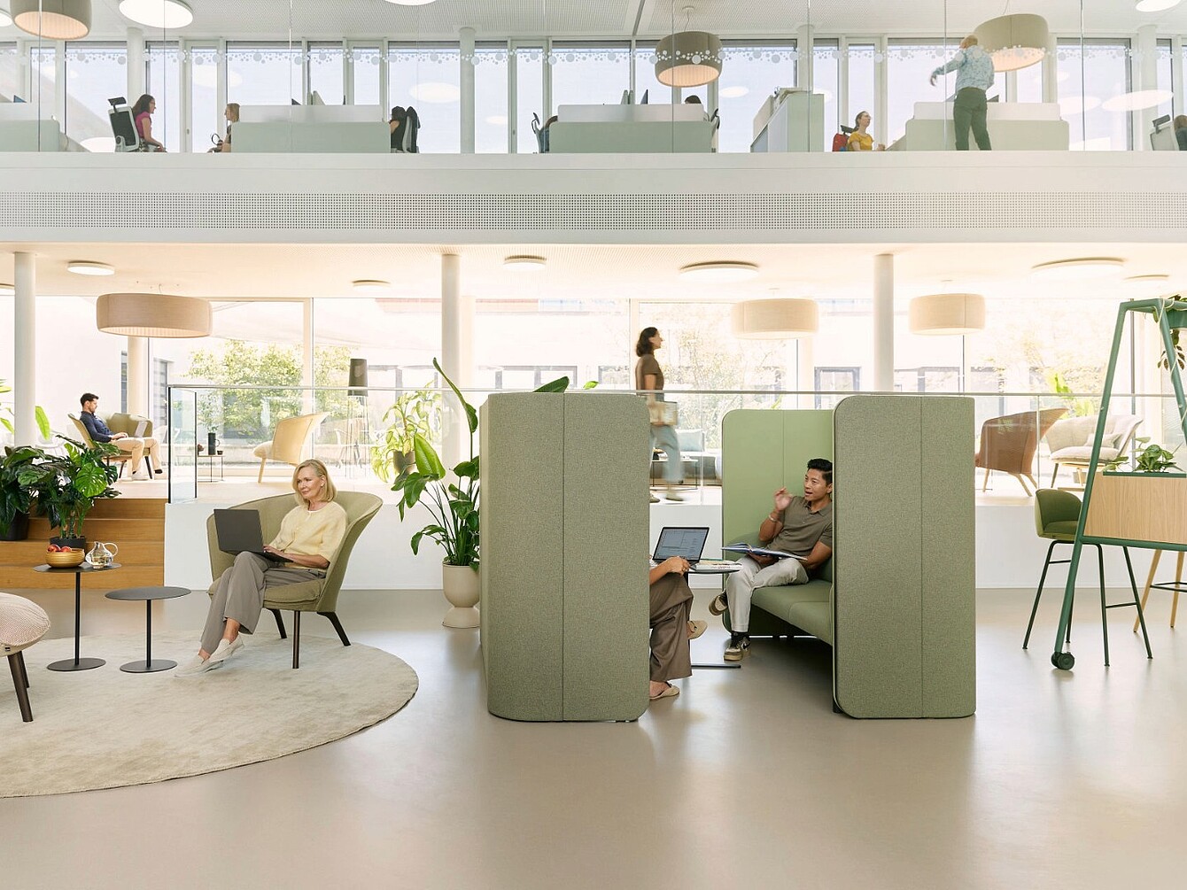 Modularer se:hive Rückzugsort mit gepolsterten Sitznischen in einem offenen, zweigeschossigen Büro mit Personen, die arbeiten und sich bewegen.