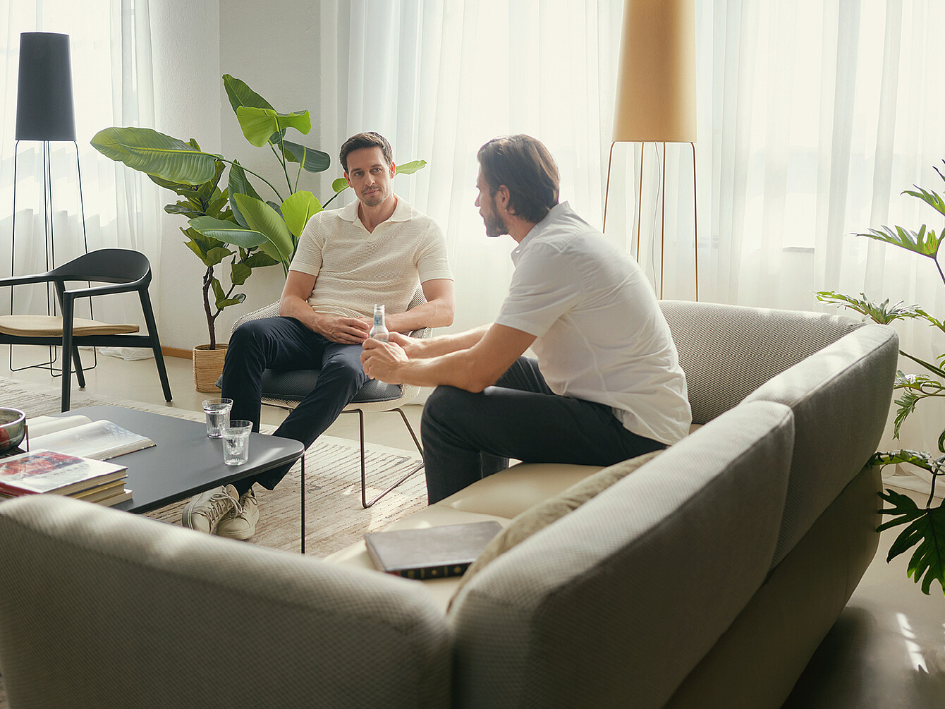 Two men having a focused conversation in a bright office lounge with modern furniture and plants, illustrating intentional in-office interaction.