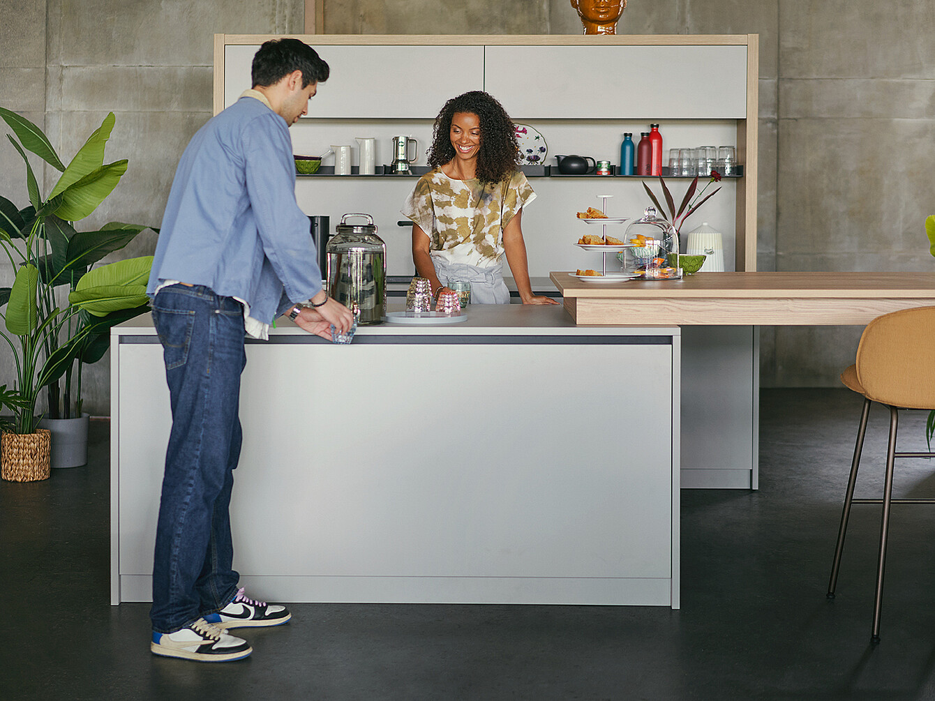 Two colleagues at a modern office kitchen counter, engaging in conversation with healthy snacks and reusable water bottles visible, illustrating sustainable catering and modern work culture.