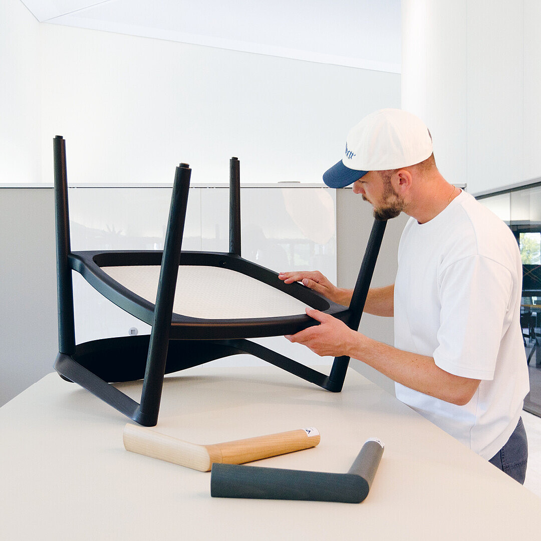 Designer Konstantin Thomas examining the underside of a black se:café wooden chair in a modern, bright workspace
