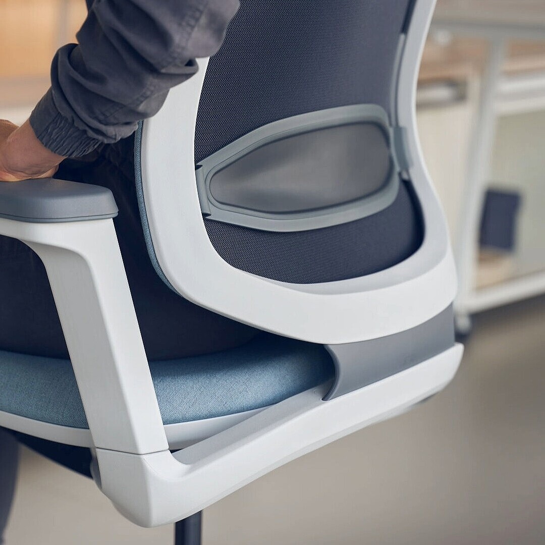 Person sitting on an office chair with visible lumbar support and armrest, hand resting on the armrest
