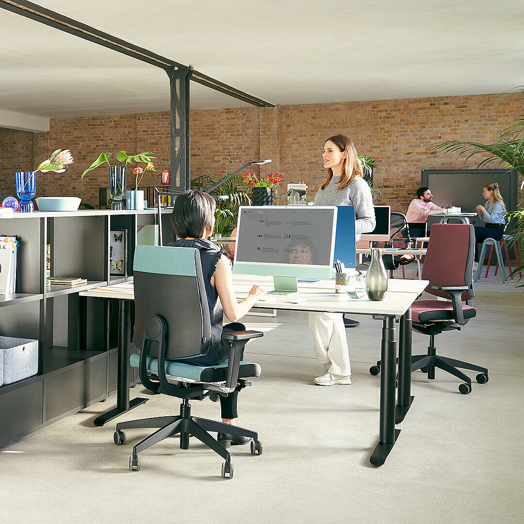 Modern open office with employees seated on Sedus black dot chairs featuring dorsokinetic backrest mechanisms, working at white desks with computers and office supplies