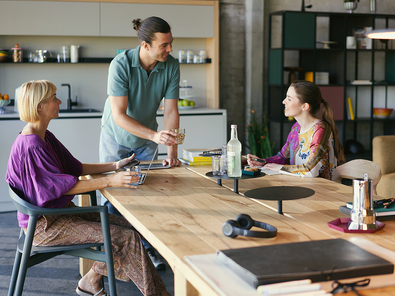 Three colleagues sharing a healthy meal and drinks in a modern office kitchen, highlighting sustainable catering and work culture.