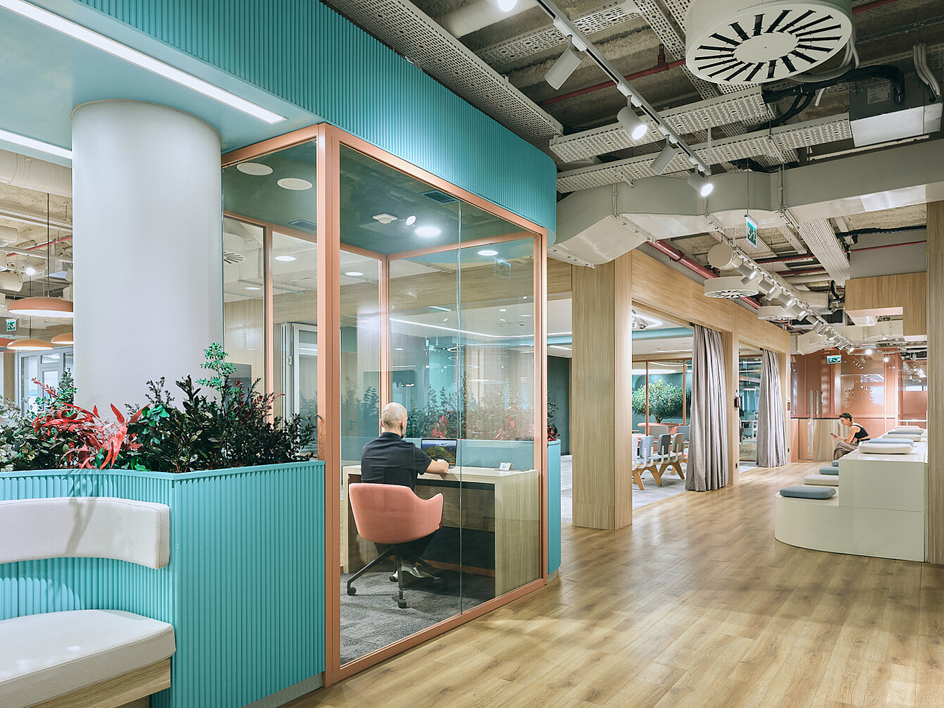 Open-plan office interior at Ford Otosan headquarters in Izmit with glass-walled meeting room, wooden flooring, seating areas, and visible ceiling ducts