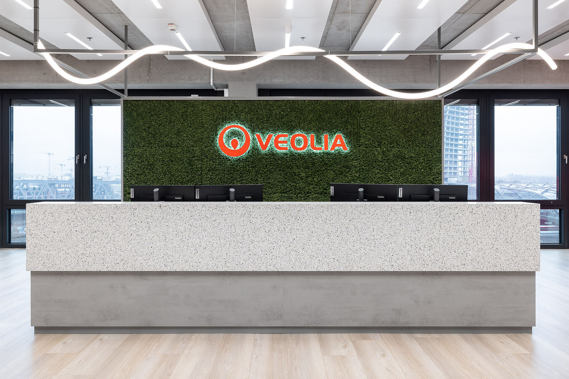 Moderner Empfangsbereich mit großem weißen Tresen vor einer grünen Wand mit dem leuchtenden Veolia-Logo.