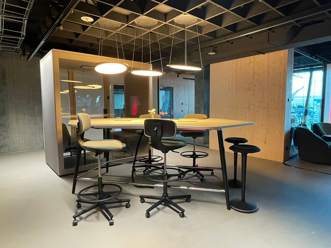 Moderner Besprechungsbereich im Novu Campus am Züricher Flughafen mit höhenverstellbarem Tisch, mehreren ergonomischen Sedus Bürostühlen und Pendelleuchten.