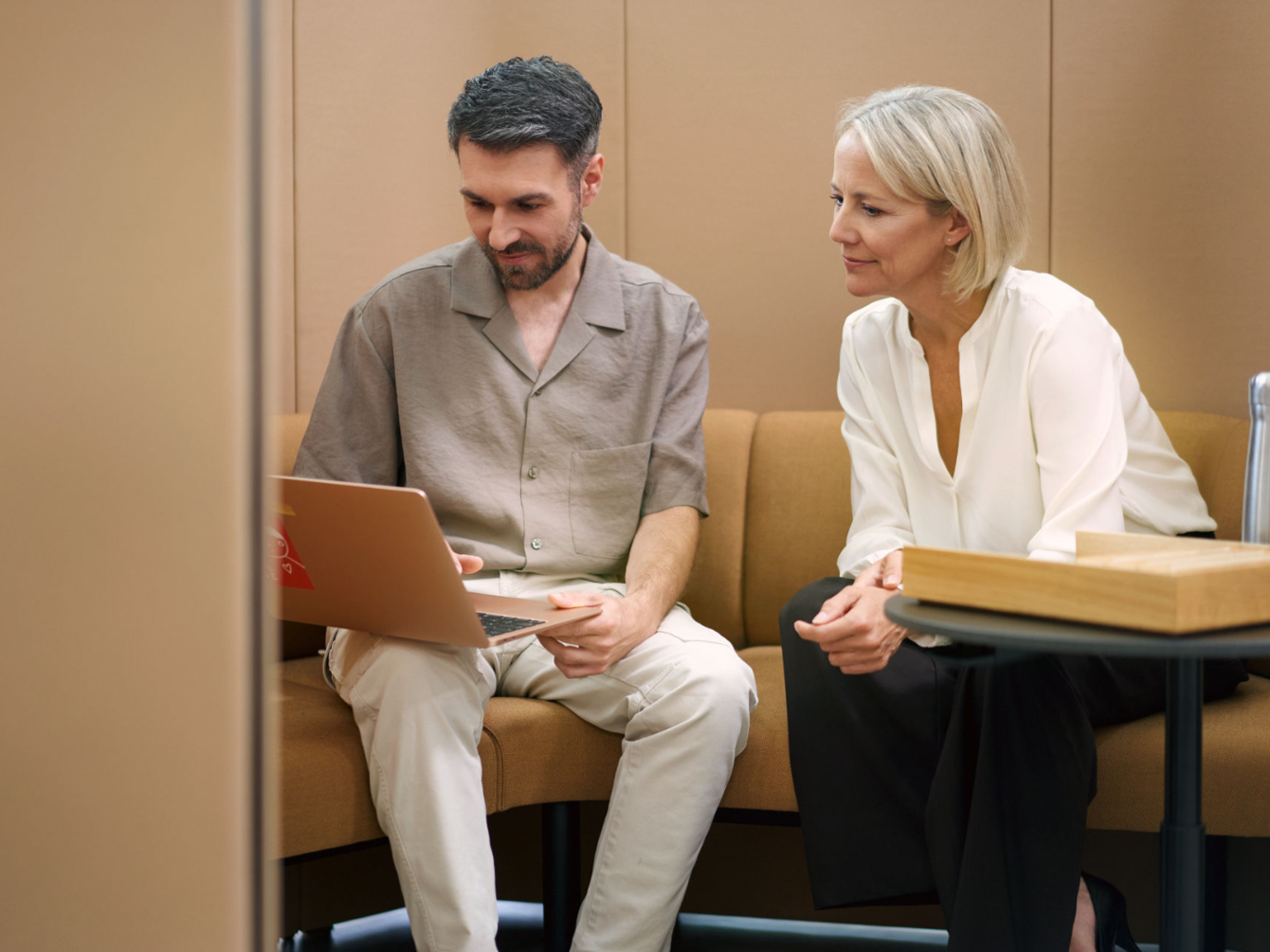 Zwei Personen sitzen nebeneinander auf einer braunen Couch und schauen auf einen Laptop 