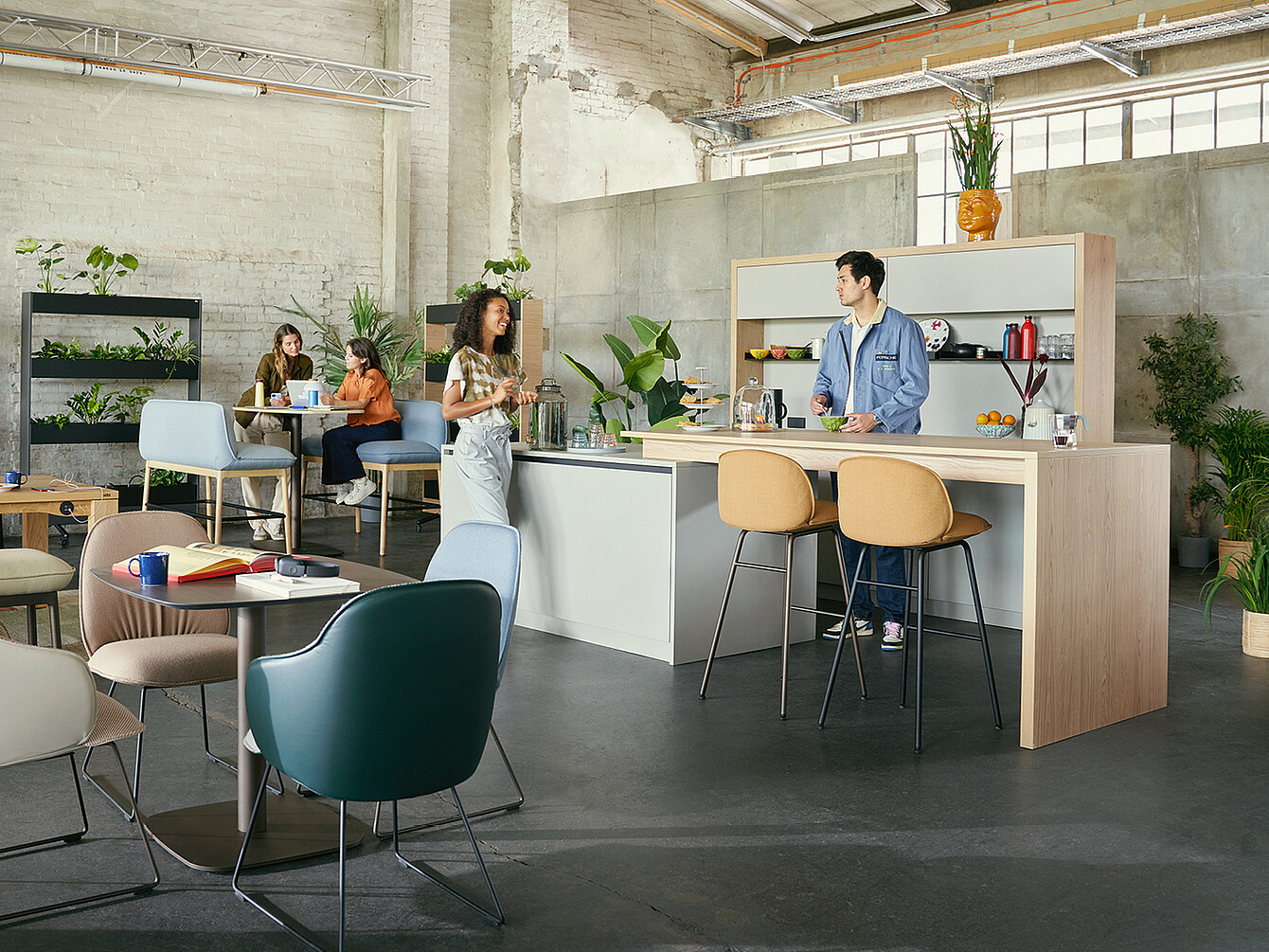 Hub Work Café office space with people collaborating, featuring a central kitchen island with stools, modern seating, and plants in an industrial-style room