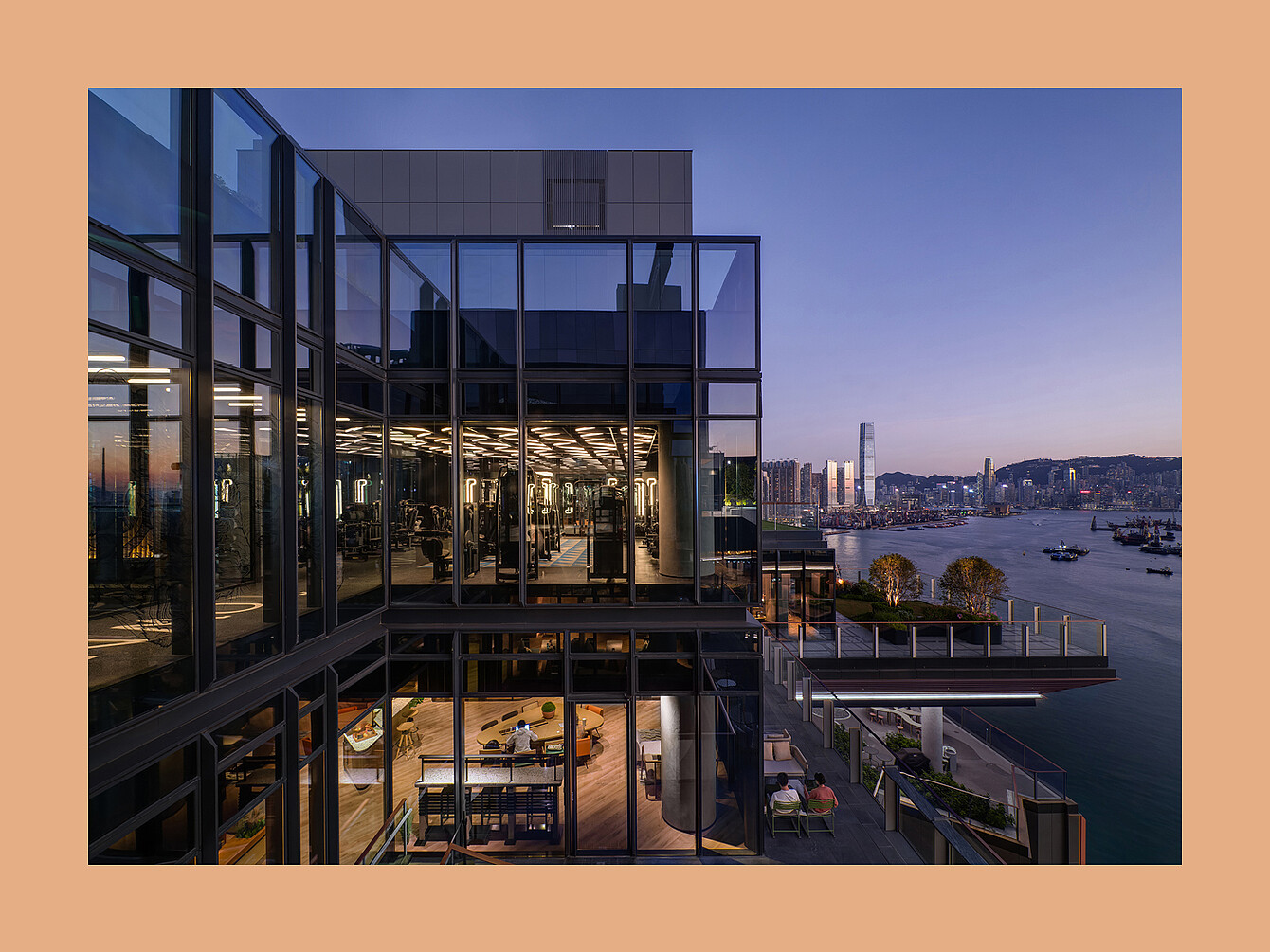 Modern multi-story building with glass walls overlooking a waterfront cityscape at dusk