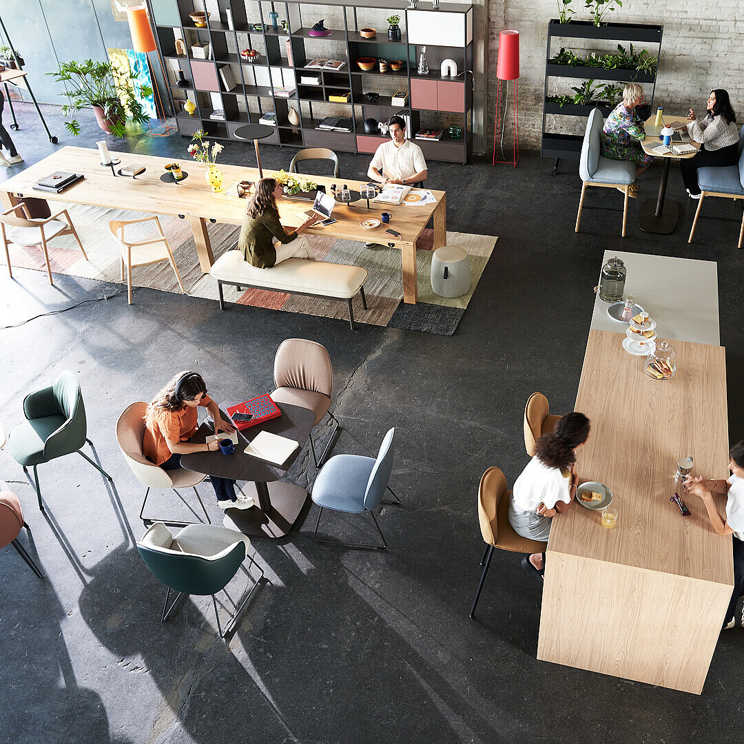 Moderner Büro-Café-Club mit verschiedenen Sitzbereichen, Menschen arbeiten und unterhalten sich in einem stilvollen, vielseitigen Raum mit viel Tageslicht.