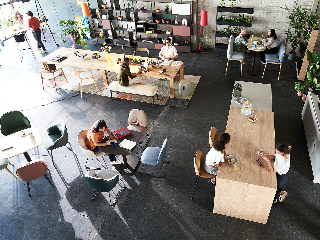Modernes Büro mit verschiedenen Sitzbereichen, Tischen und Pflanzen, Menschen arbeiten und unterhalten sich in einem inspirierenden, multifunktionalen Raum