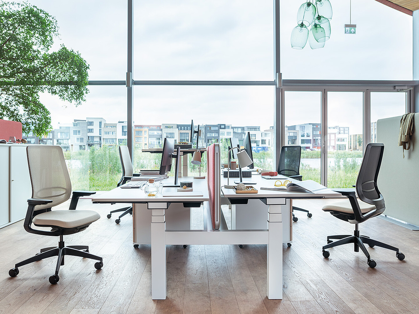 Modernes Büro mit vier Arbeitsplätzen, ergonomischen Stühlen und großen Fenstern mit Blick auf Wohngebäude